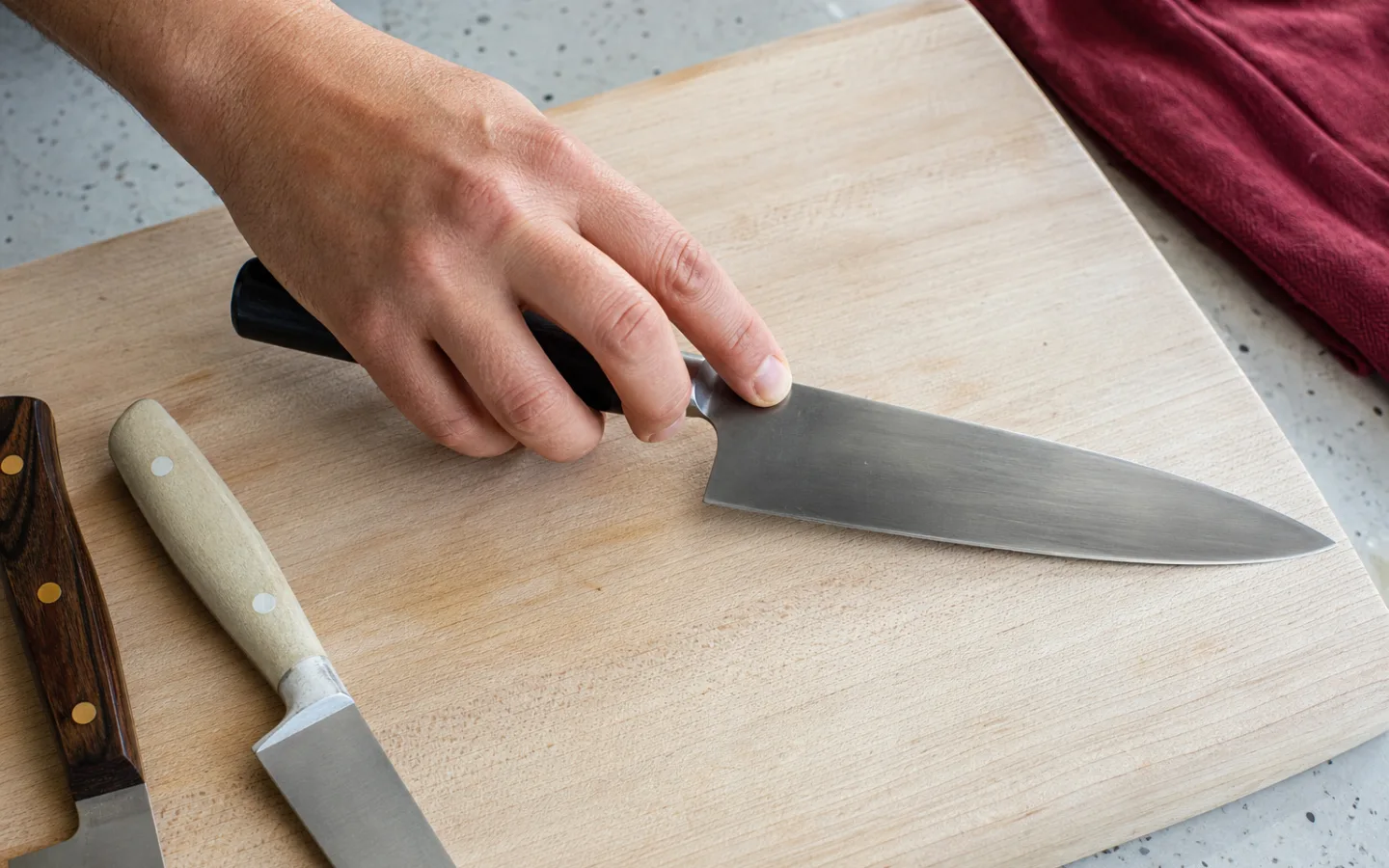 En hand som greppar en kockkniv över en träskärbräda, med två andra knivar bredvid